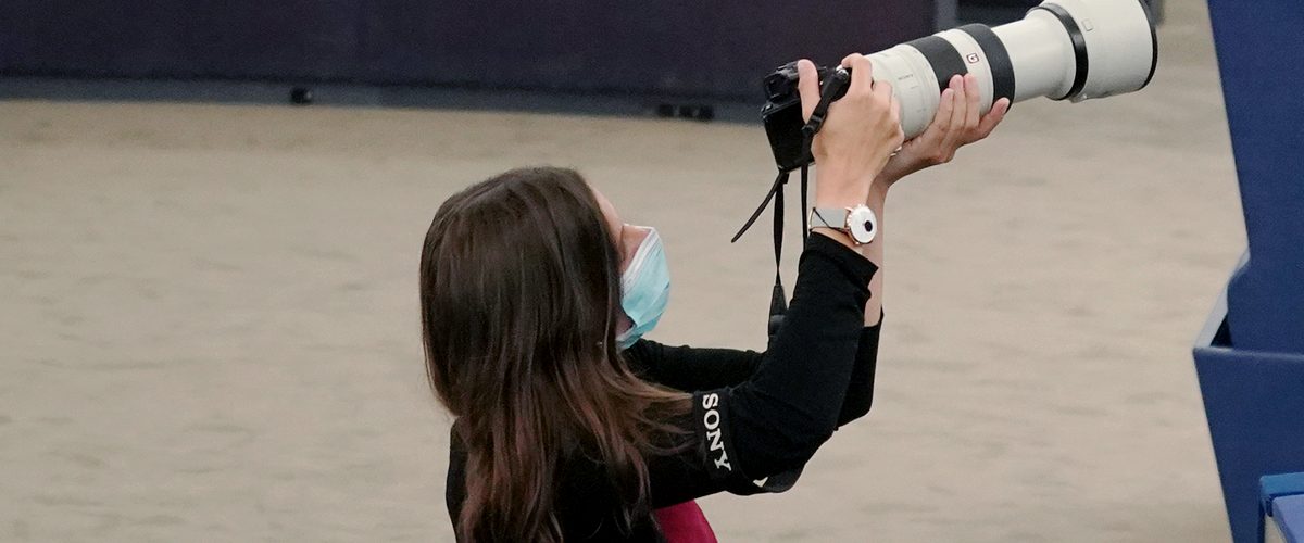 A press photographer kneeling with a Sony mirrorless camera and a long telephoto lens
